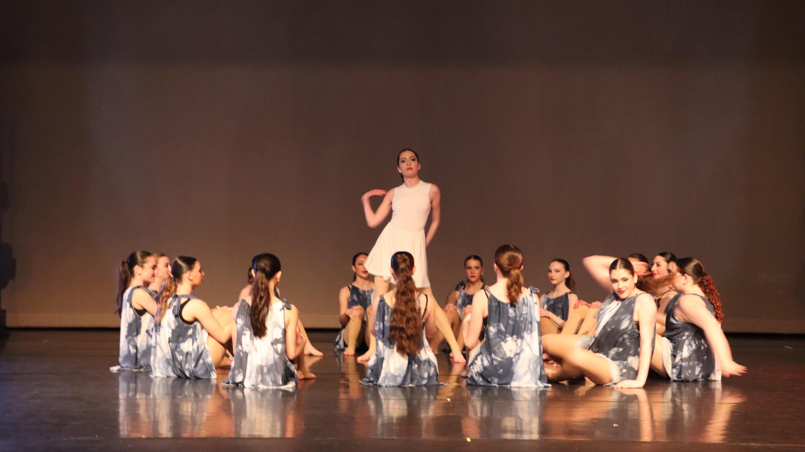 Dancers sitting in a circle with a dancer dressed in white